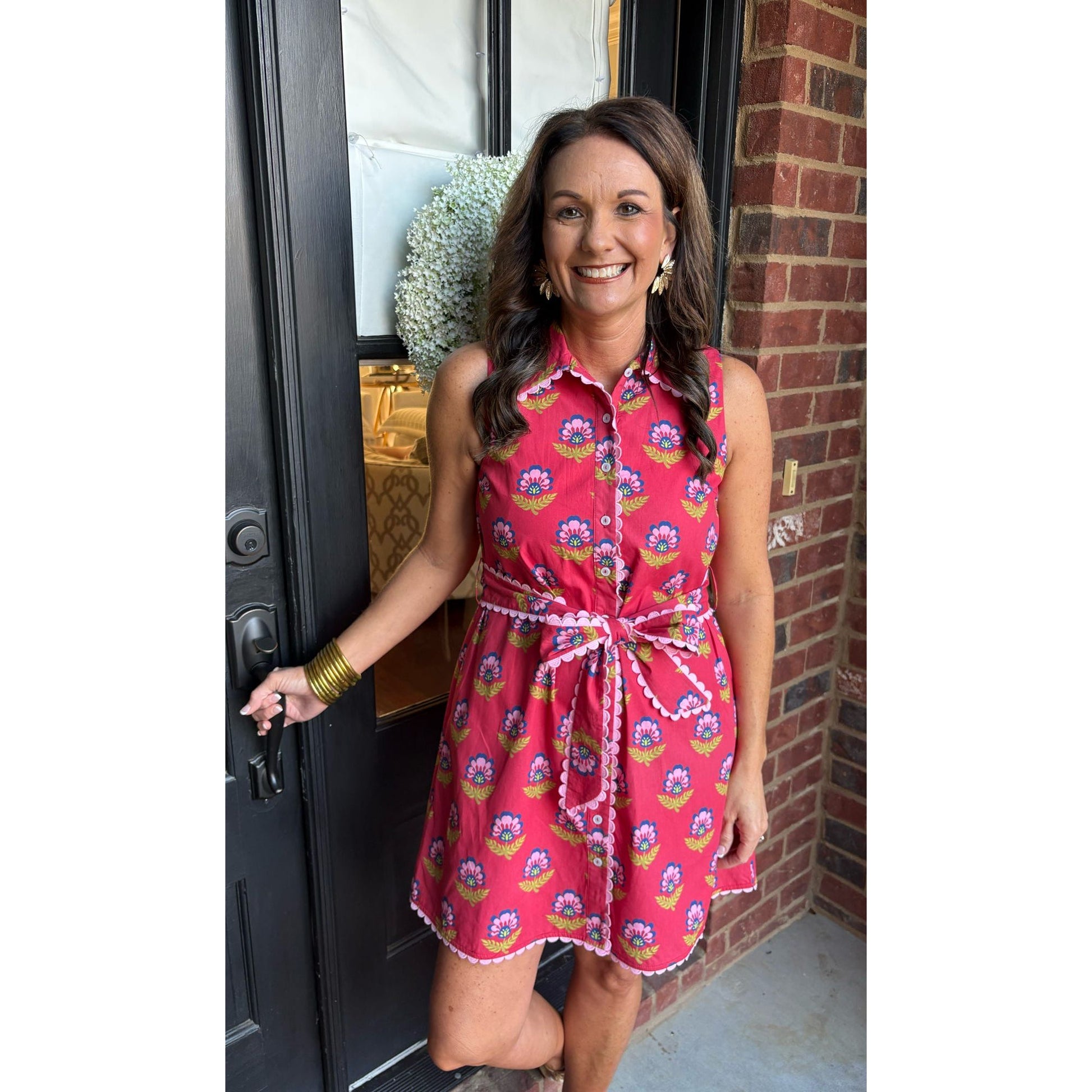 Woman in a pink floral dress standing at a door.