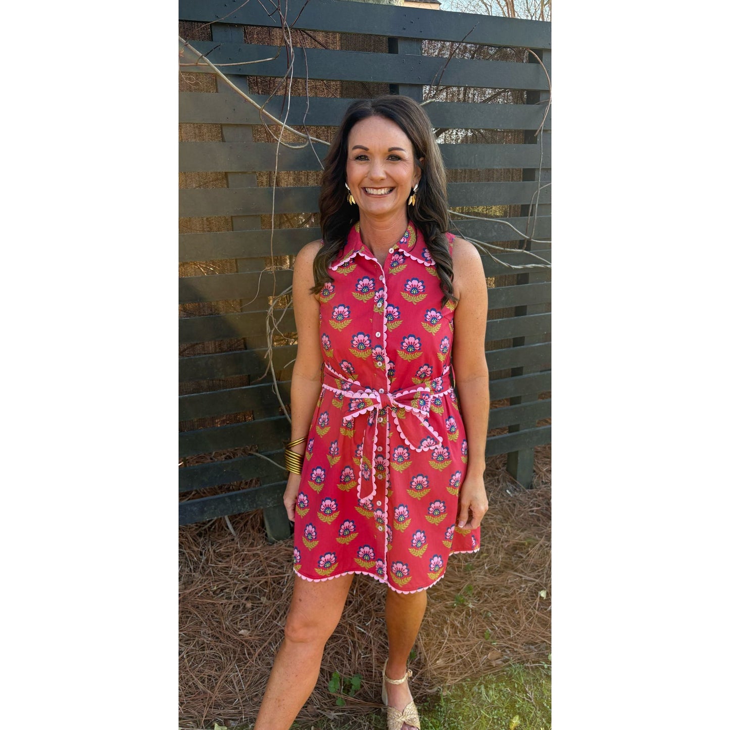 Woman wearing a red patterned dress standing in front of a wooden fence.