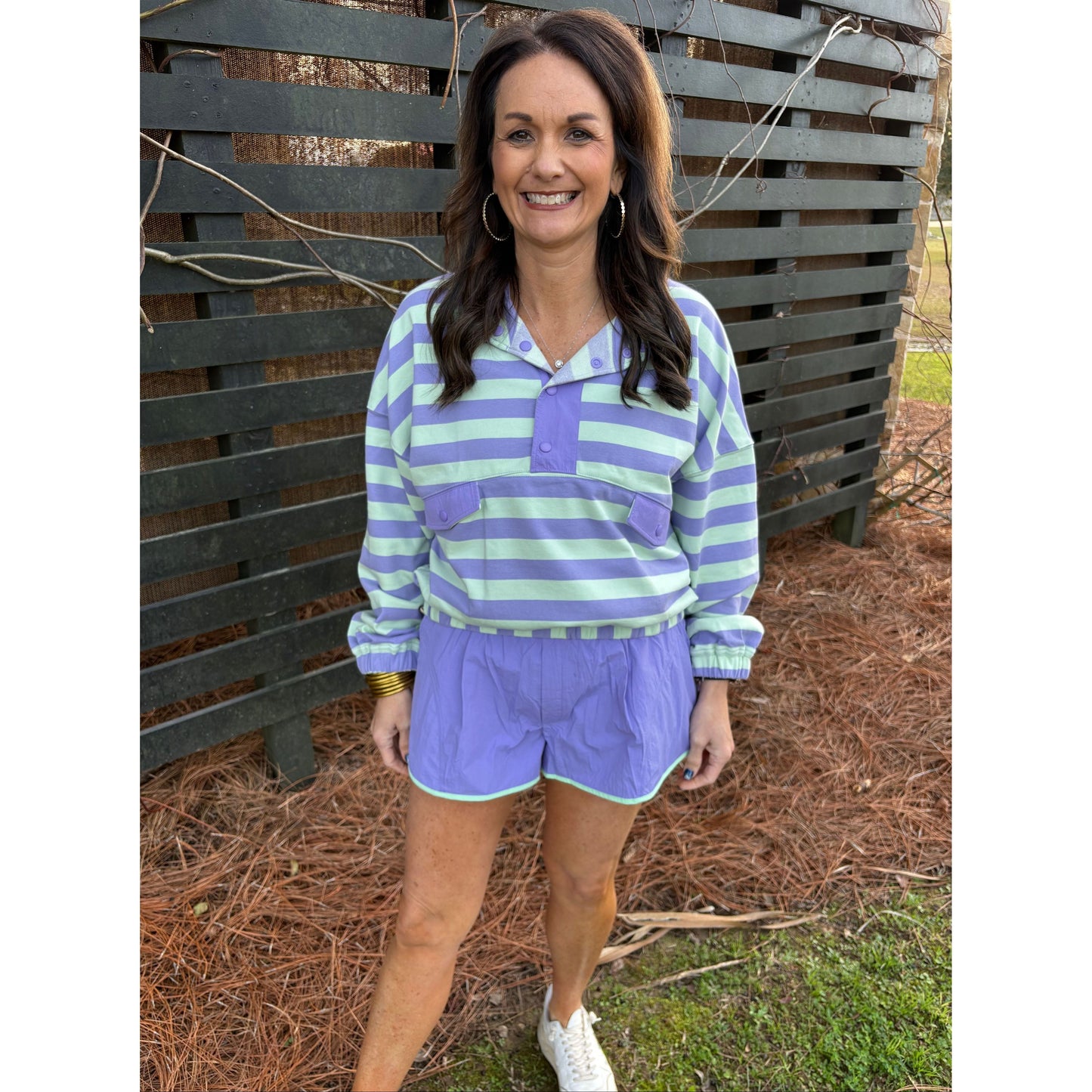 Woman wearing a purple and green striped outfit standing outdoors on a bench.