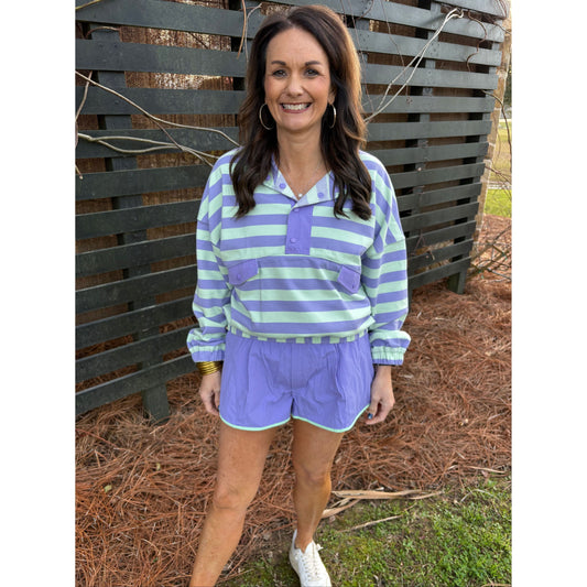 Woman wearing a purple and green striped outfit standing outdoors on a bench.