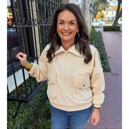 Woman wearing a beige jacket and blue jeans standing on a sidewalk.