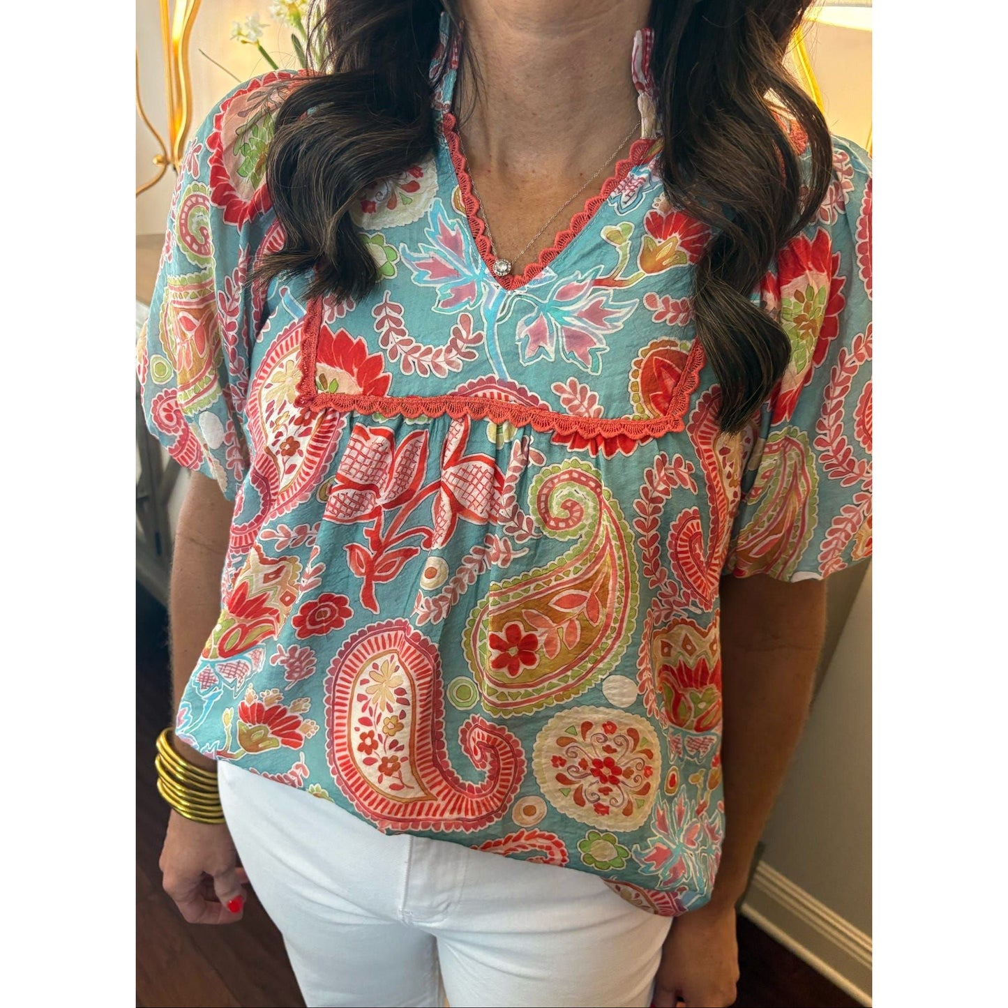 Woman wearing a colorful patterned blouse with white pants indoors.