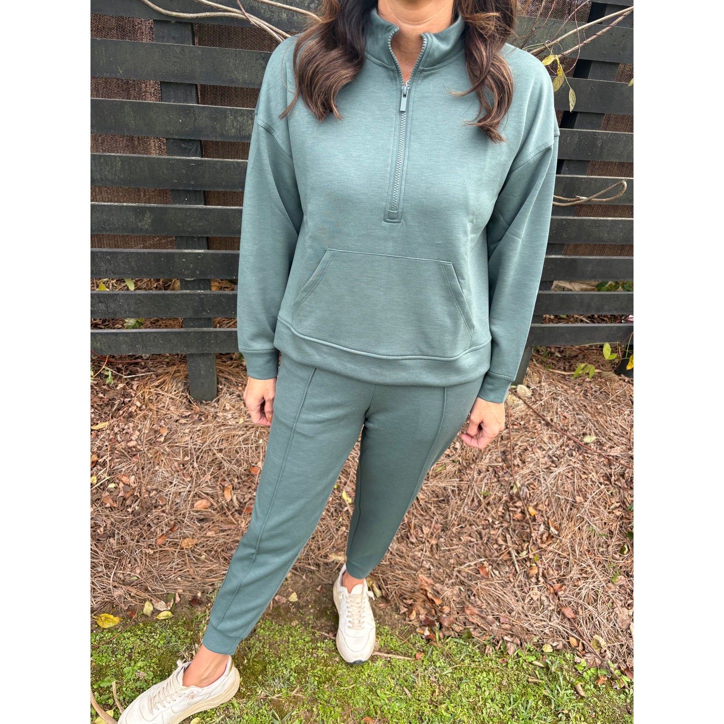 Person wearing a teal tracksuit sitting on a bench outdoors.