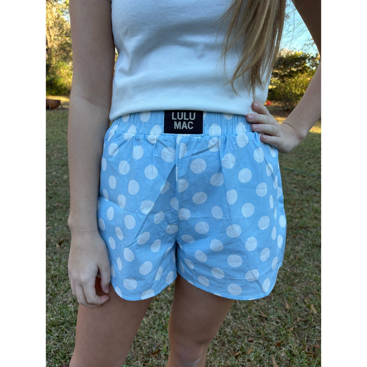 Person wearing blue polka dot shorts with Lulu Mac label outdoors