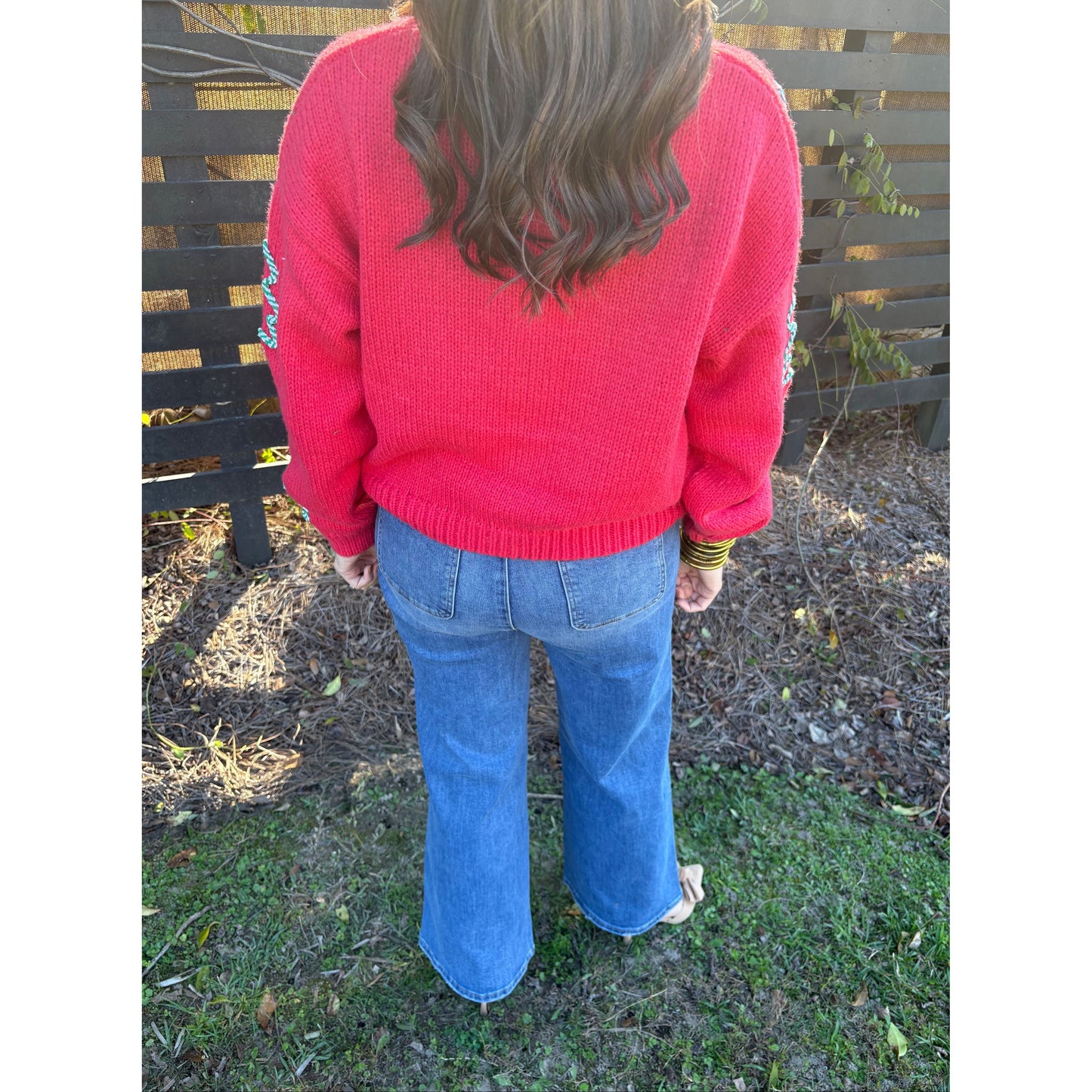 Person wearing a red sweater and blue jeans standing on grass and dirt.