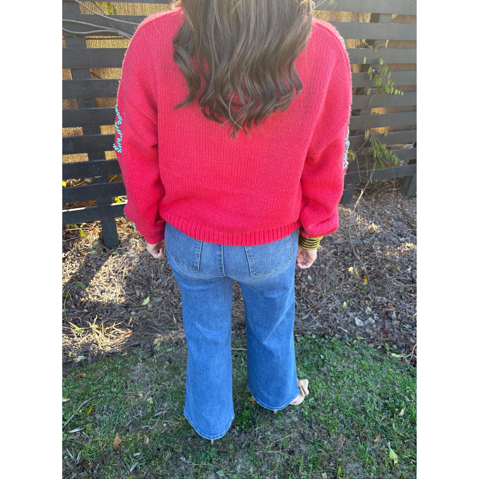 Person wearing a red sweater and blue jeans standing on grass and dirt.