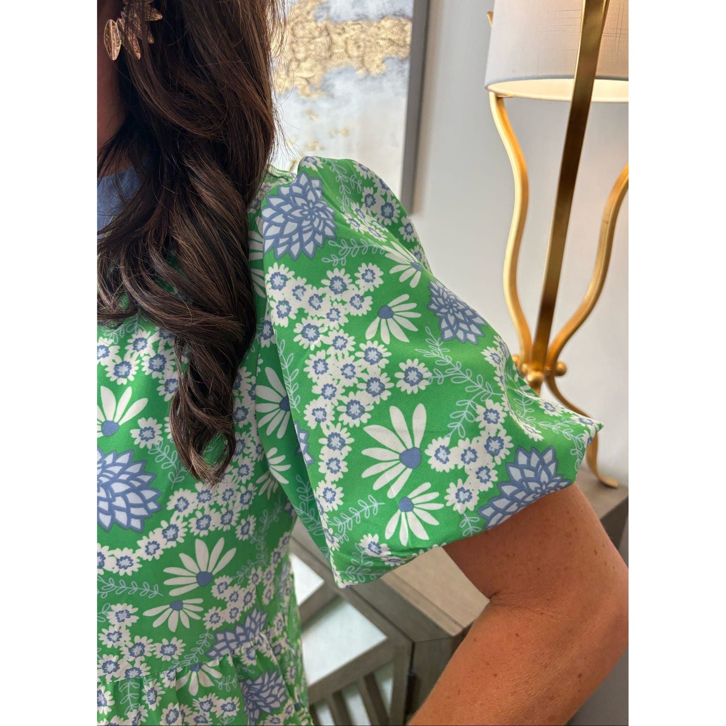 Person wearing a green floral dress with a lamp and decorative wall in the background