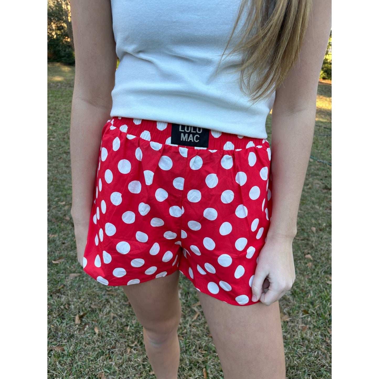 Person wearing red polka dot shorts with a visible brand label outdoors.