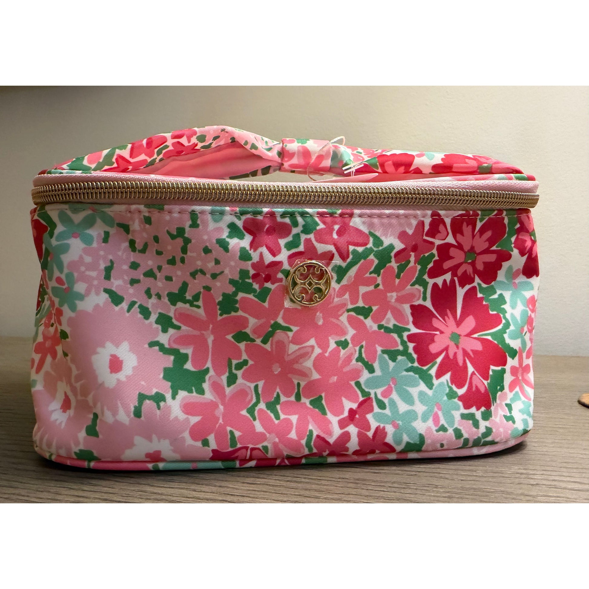 Floral-patterned cosmetic bag with a visible brand logo on a wooden surface.