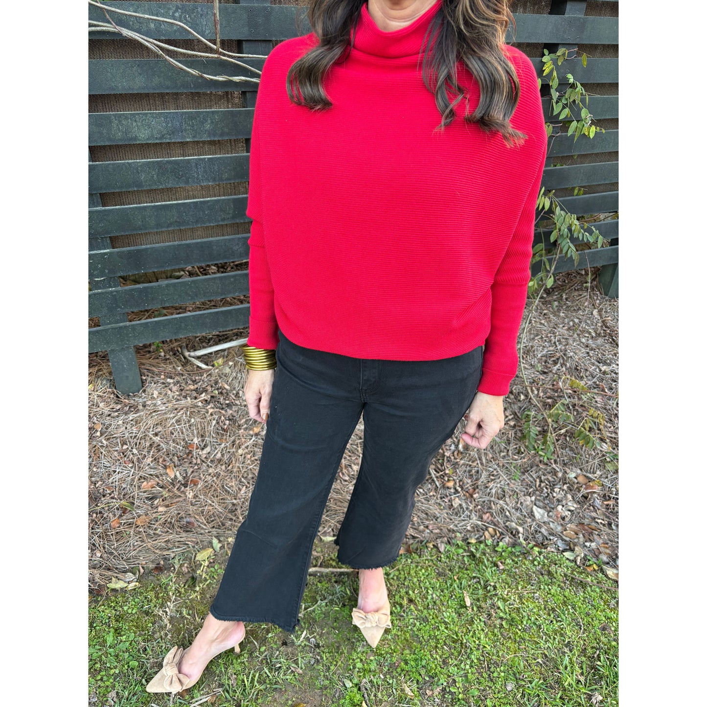 Person wearing a red sweater and black pants sitting on a bench outdoors.