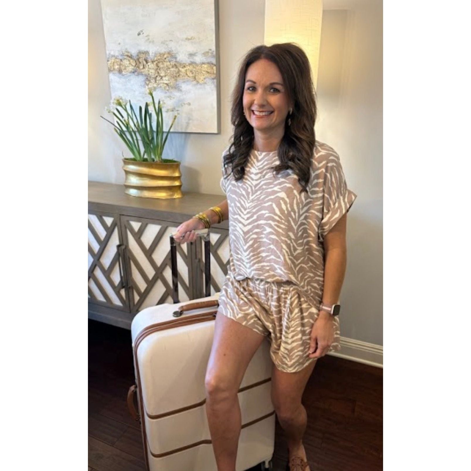 Woman in a gold and white patterned outfit standing next to a suitcase in a room with decorative elements.