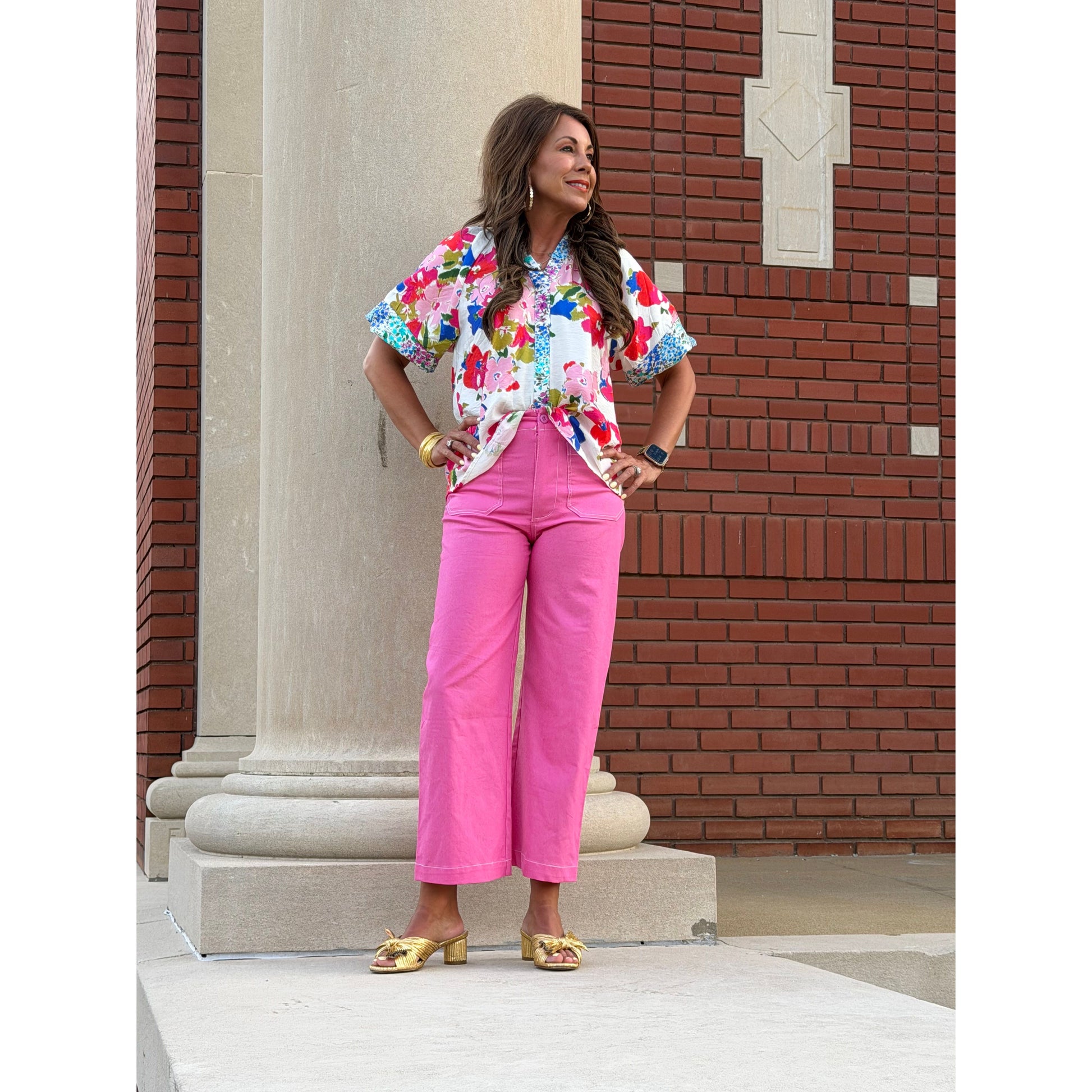 Woman in a colorful floral blouse and pink pants standing on a stone step.