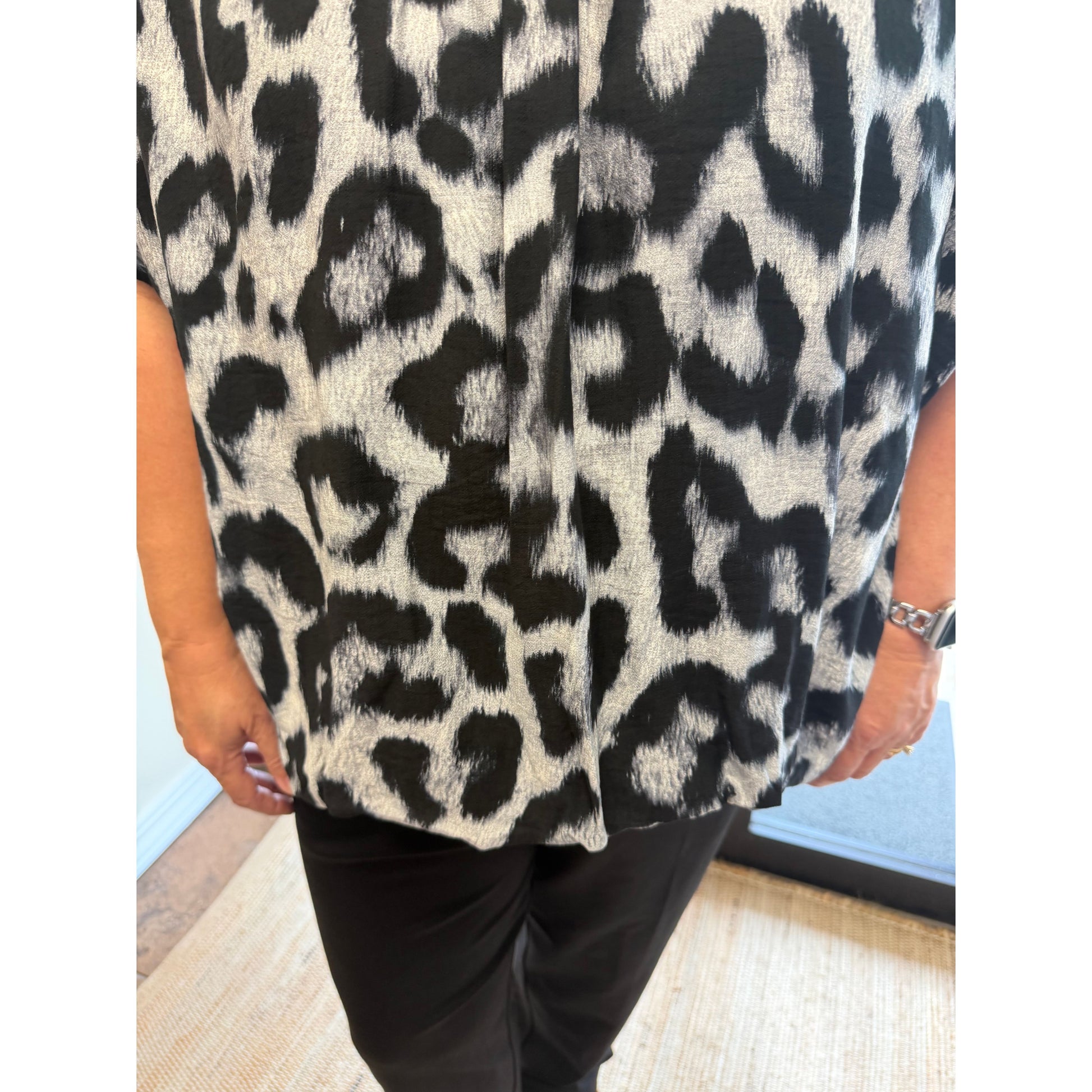 A close-up of a person wearing a short-sleeve leopard print top with black and off-white spots, paired with black pants.