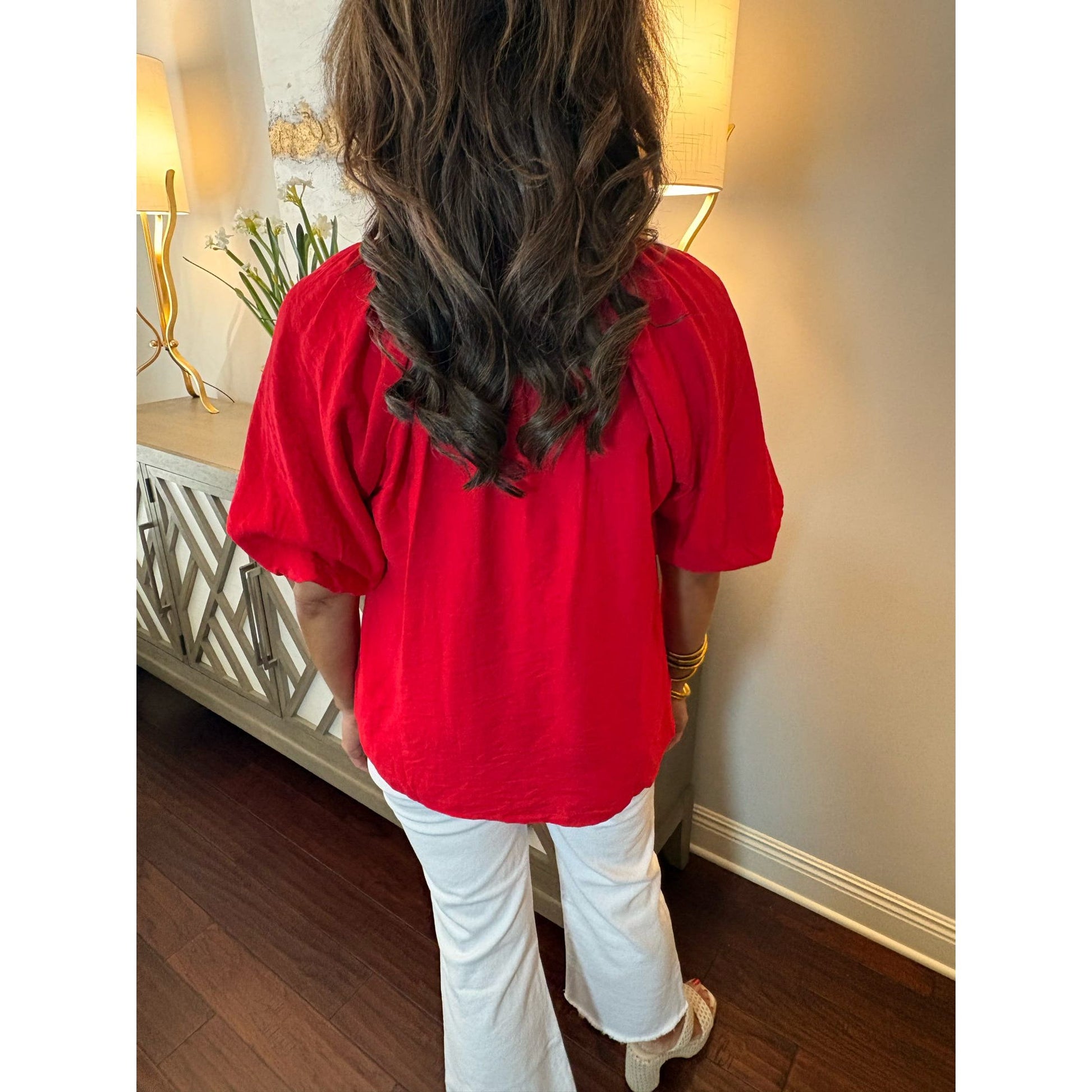 Person wearing a red blouse and white pants in a room with lamps and decor.
