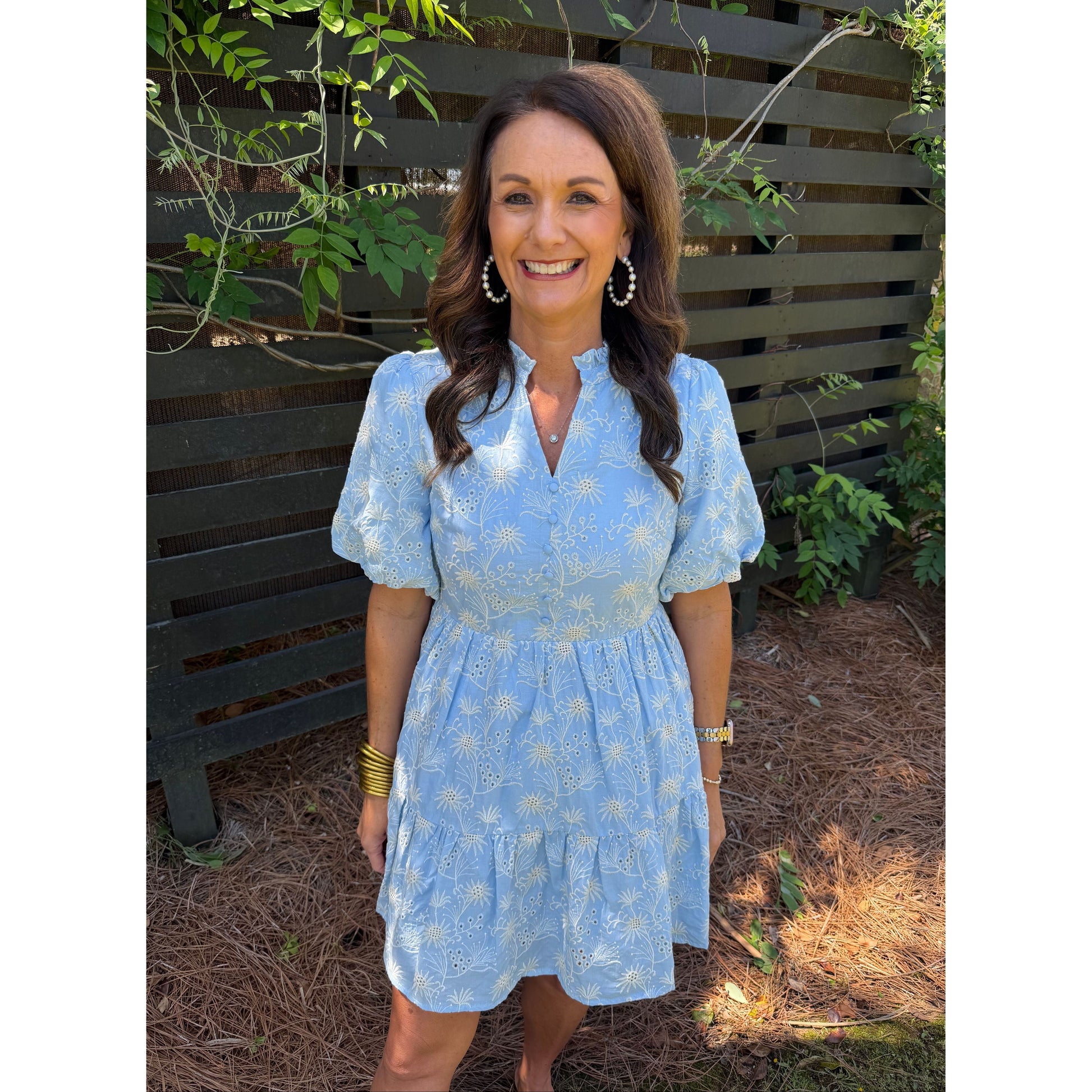 Woman in a blue dress standing outdoors with greenery around