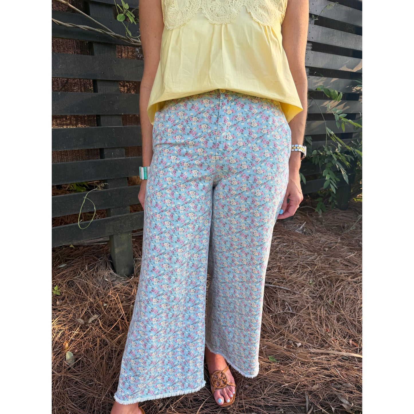 Person wearing a yellow top and light blue floral pants standing outdoors.