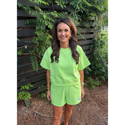 Woman wearing a bright green outfit standing outdoors with plants in the background