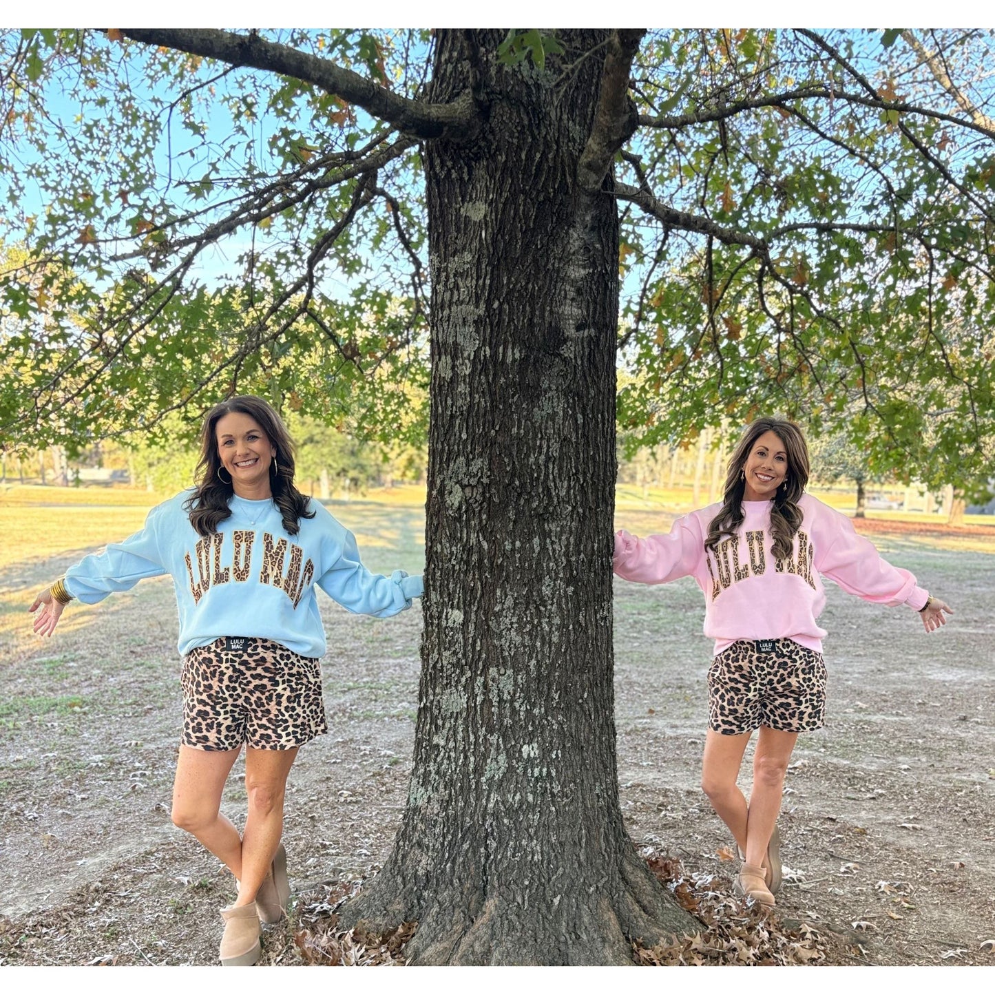 Two women in matching outfits standing next to a tree outdoors.