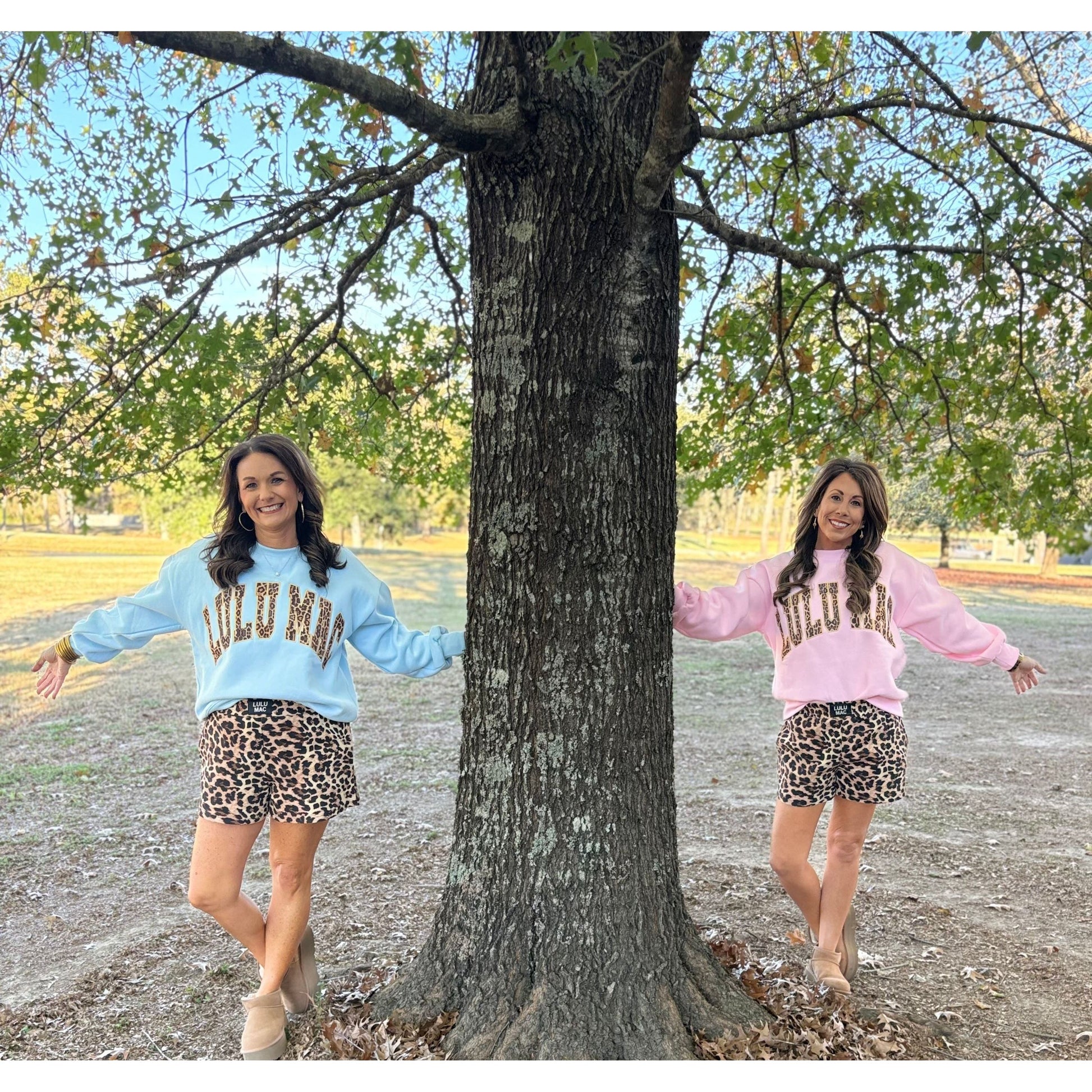Two women in matching outfits standing next to a tree outdoors.