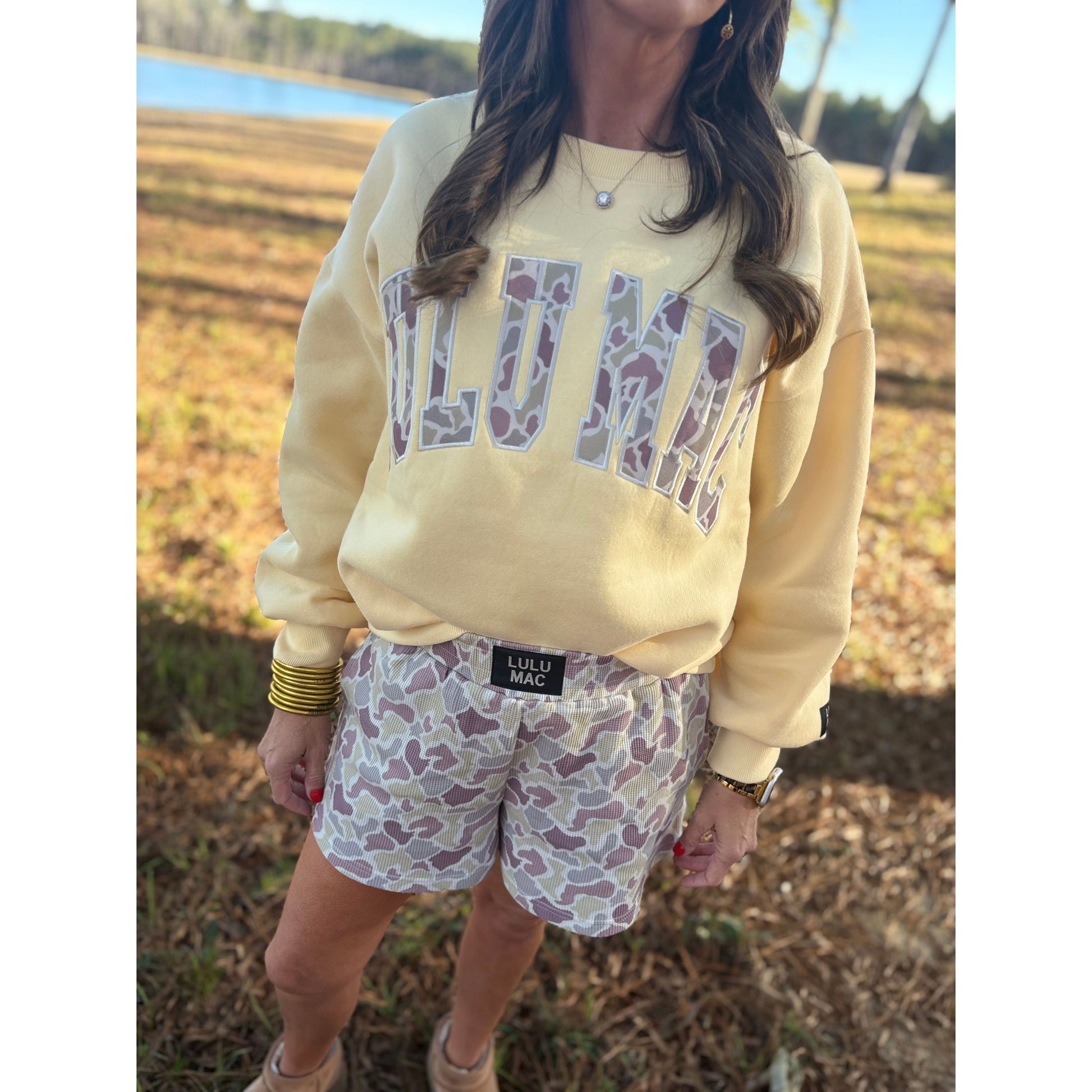 Person wearing a yellow sweatshirt with 'Lulu Mac' text and patterned shorts outdoors.