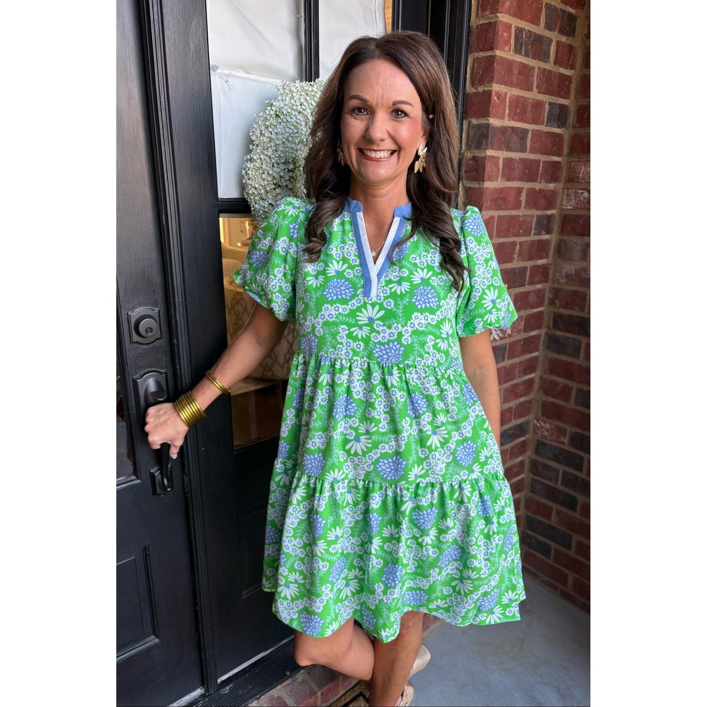 Woman in a green floral dress standing at a door.