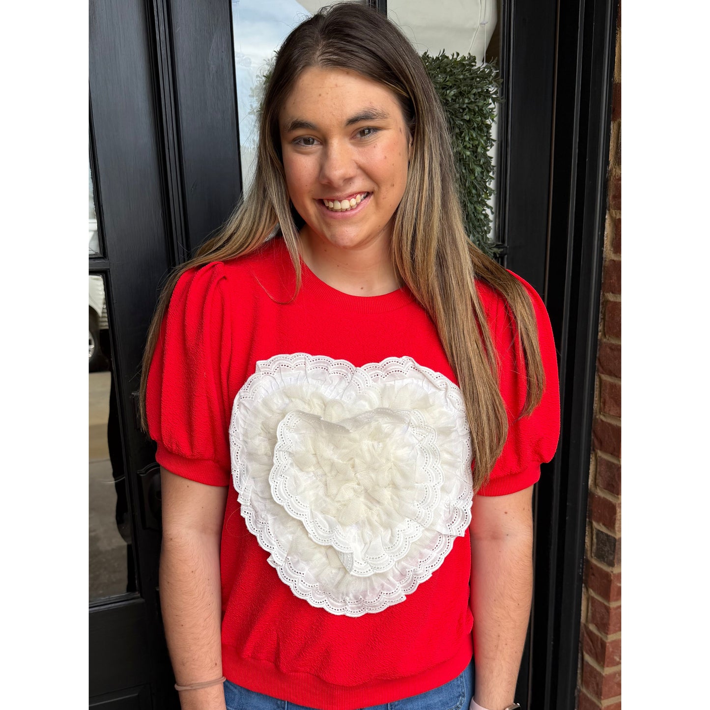 Woman standing in front of door with red heart shirt on. 