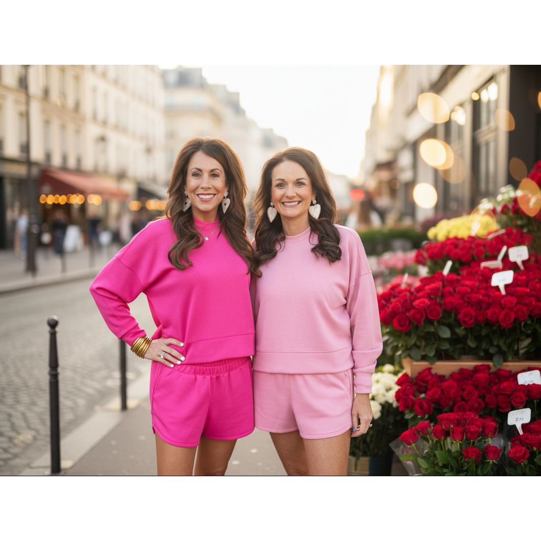 Two women in pink outfits standing on the street by a flower market.