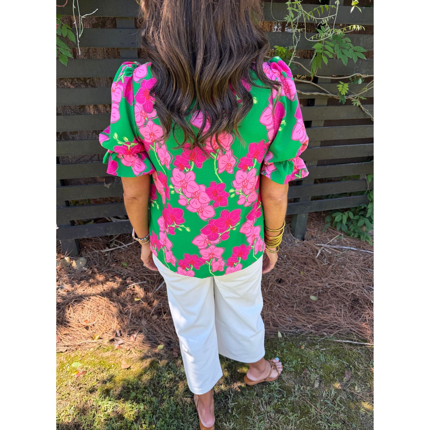 Person wearing a green and pink floral dress with white pants in an outdoor setting.