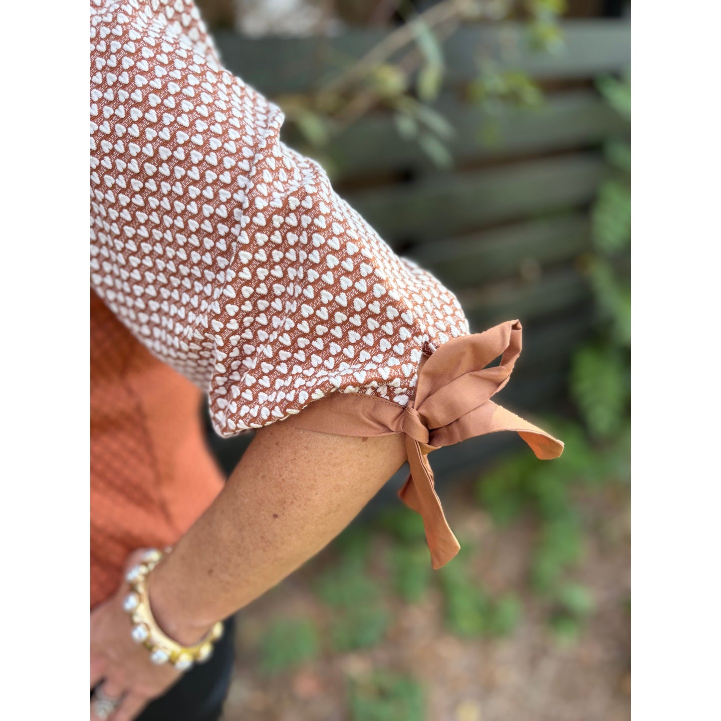 Close-up of a person wearing a patterned sleeve with a bow, blurred green background