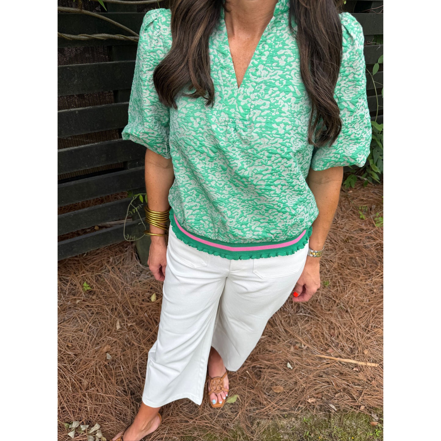 Person wearing a green floral top and white pants sitting on the ground.