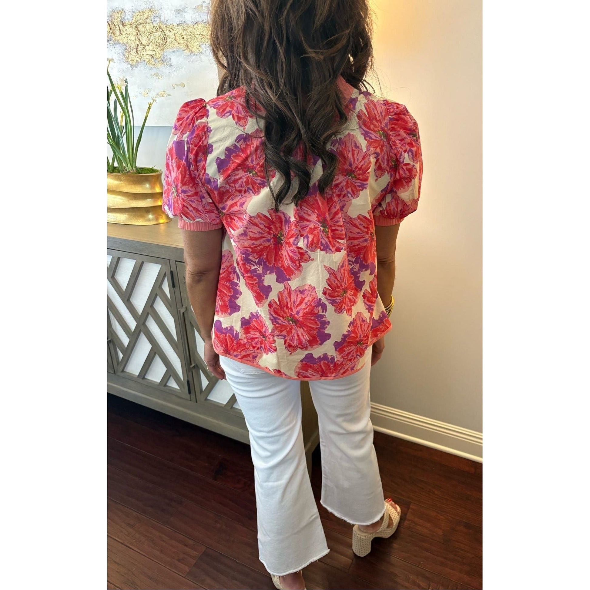 Person wearing a floral blouse and white pants in an indoor setting.