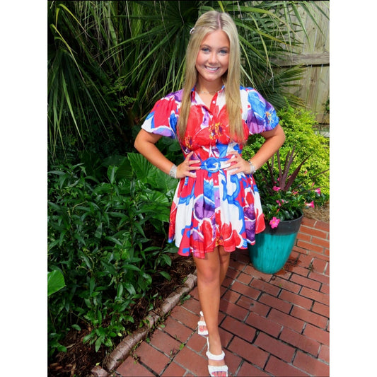 Woman in a colorful dress standing outdoors with plants and a brick path in the background