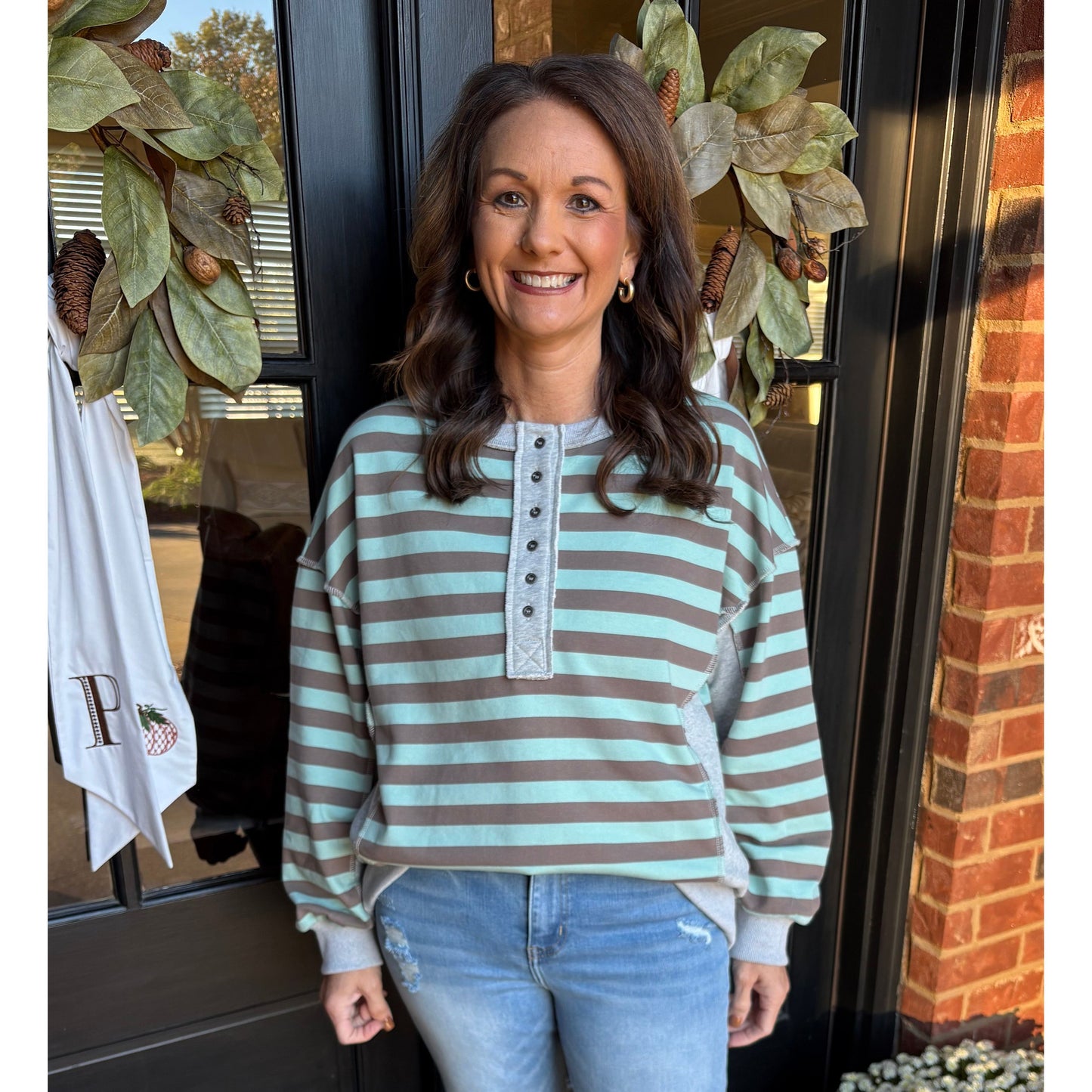 Woman wearing a striped sweater and jeans standing in front of a door with decorative elements.
