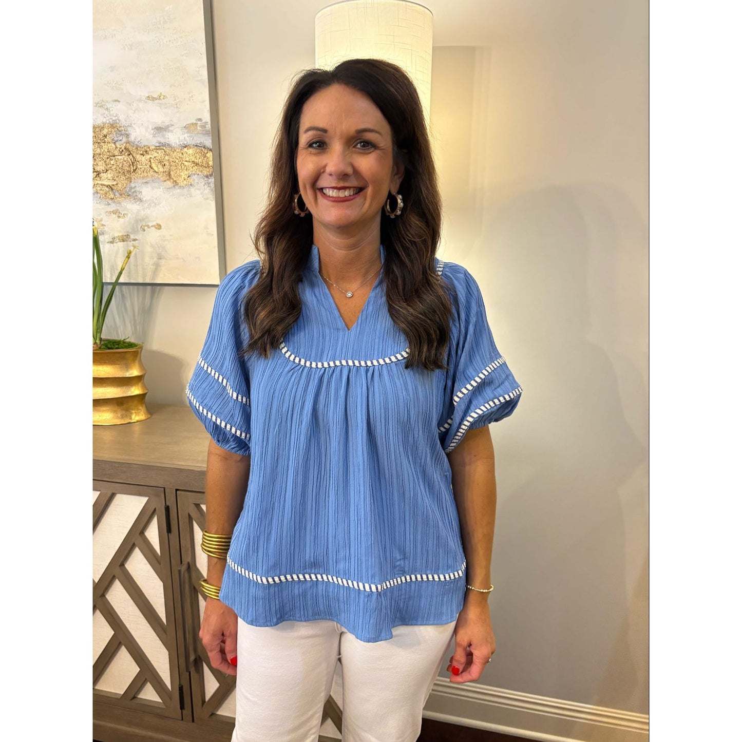 Woman wearing a blue blouse with white trim in a room with decorative elements.