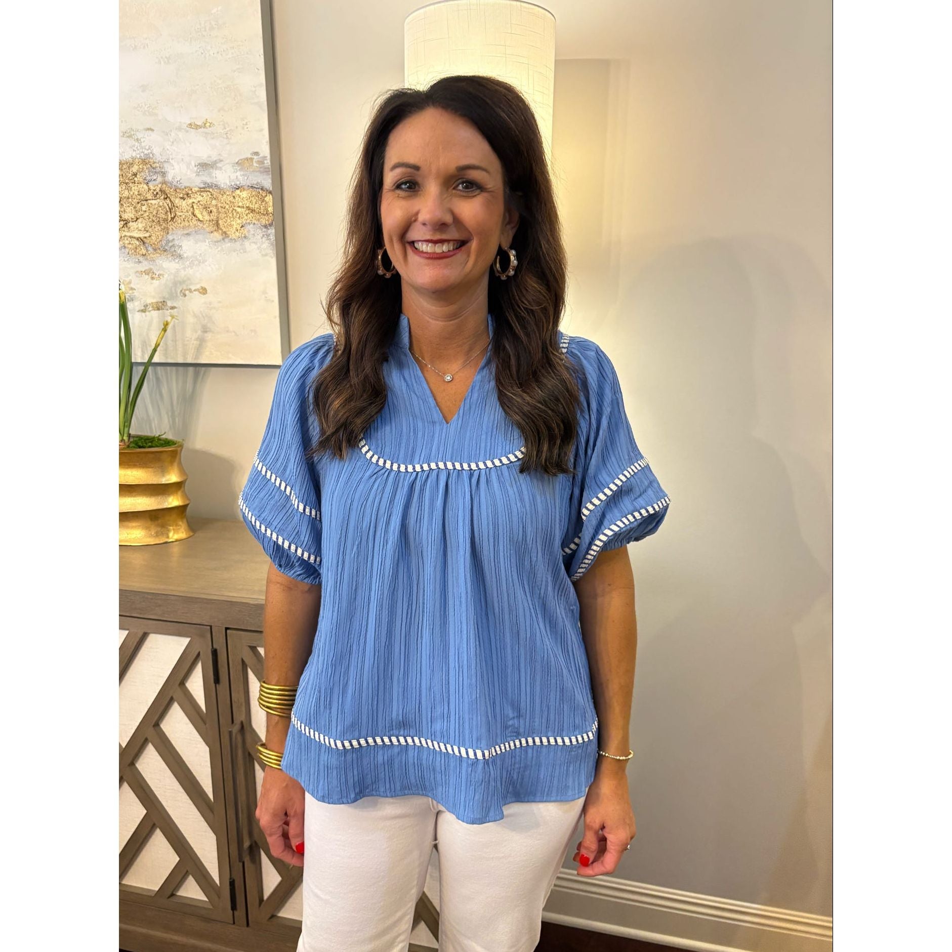 Woman wearing a blue blouse with white trim in a room with decorative elements.
