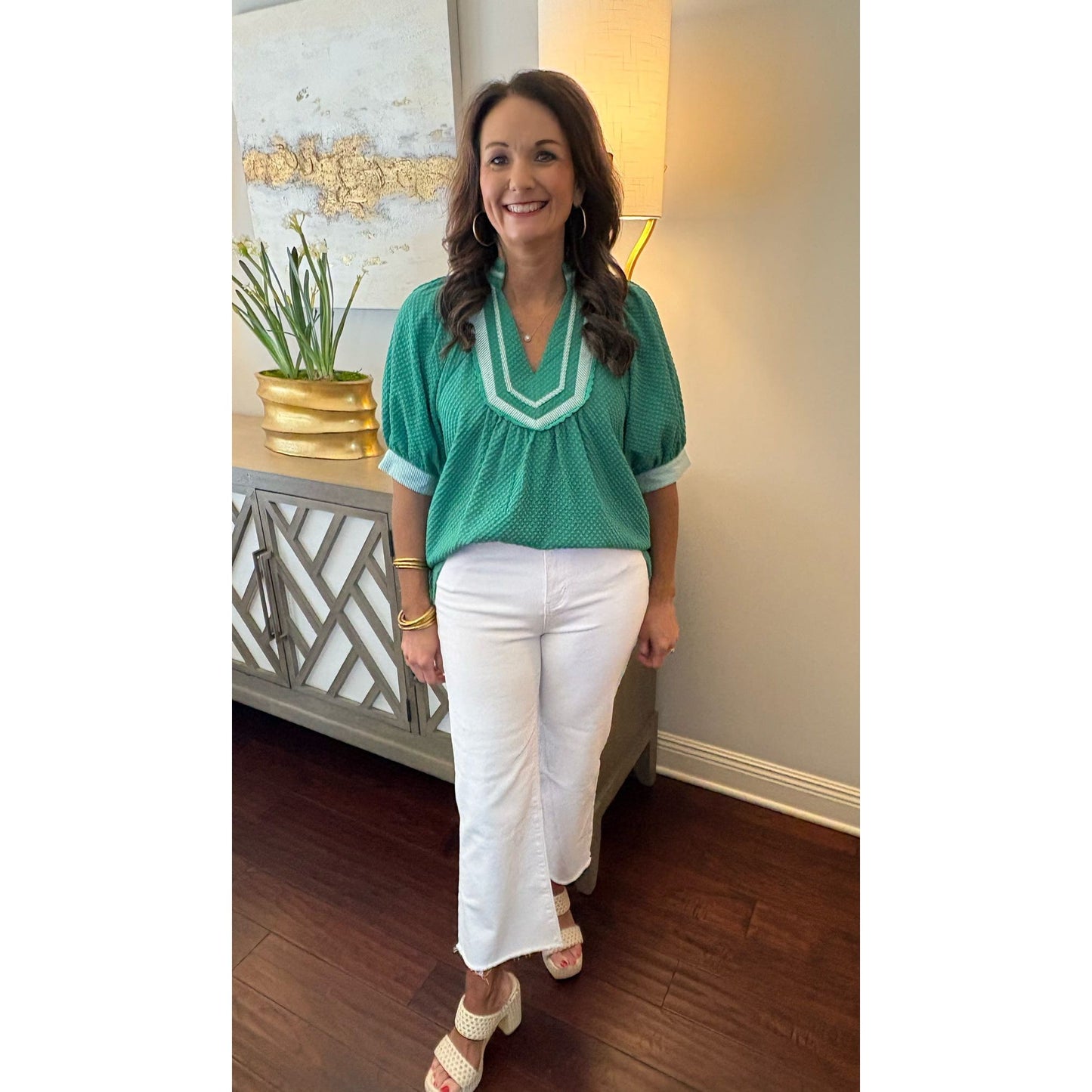 Woman in a green top and white pants standing in a room with decorative elements.