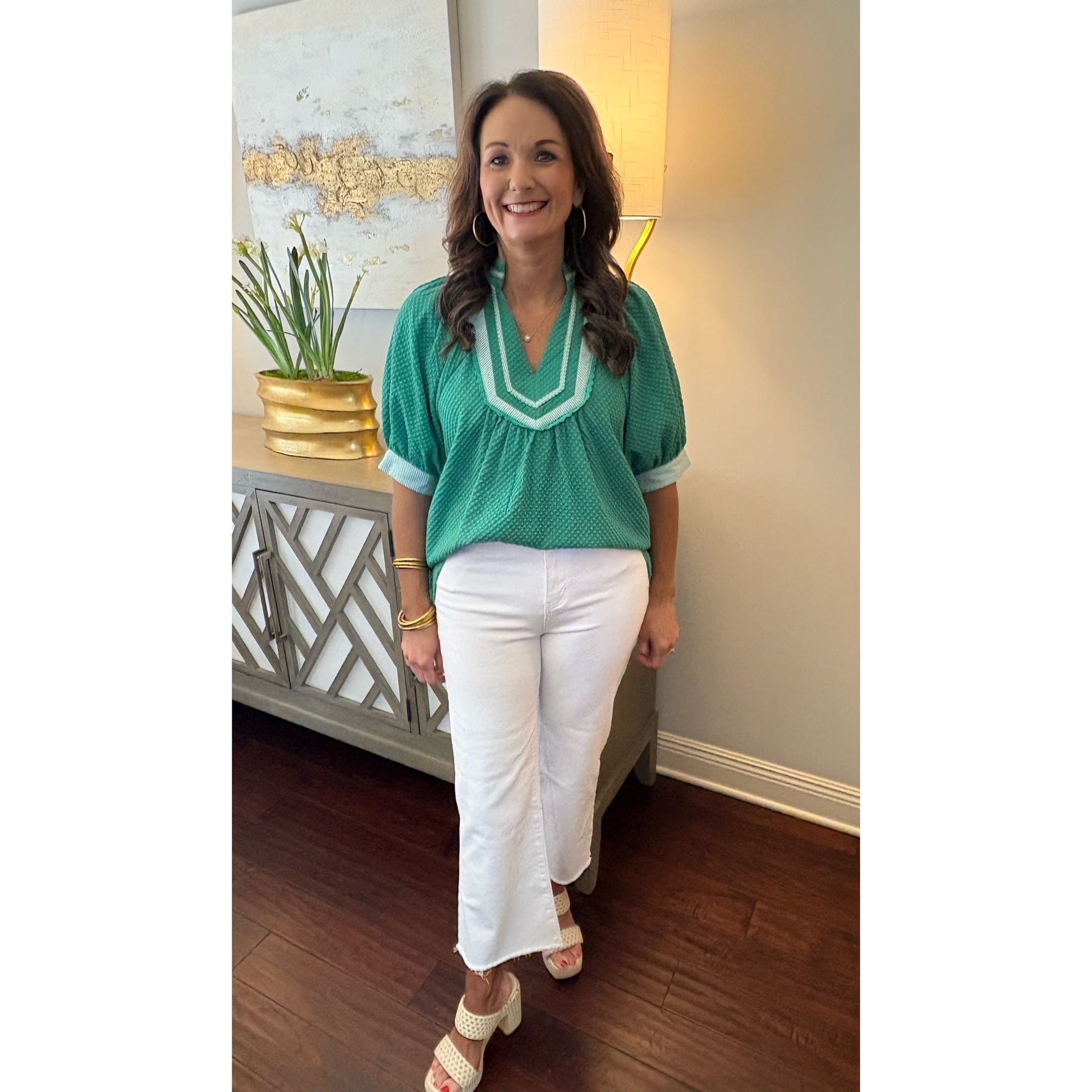 Woman in a green top and white pants standing in a room with decorative elements.