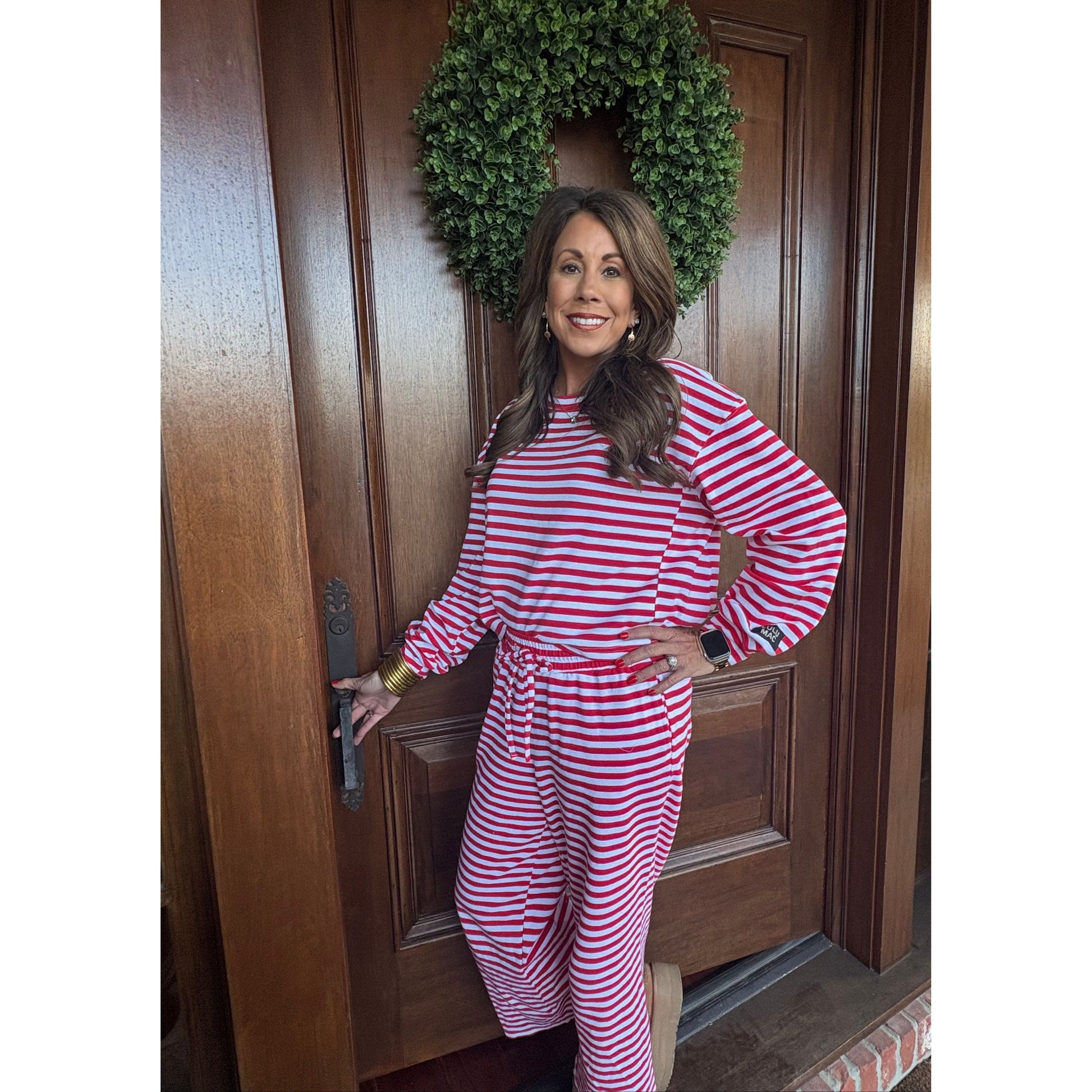 Woman in red and white striped dress standing on a wooden door with a wreath beside her.