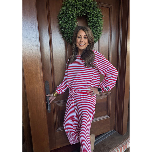 Woman in red and white striped dress standing on a wooden door with a wreath beside her.
