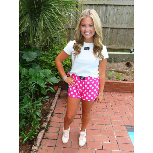 Woman wearing a white t-shirt and pink polka dot shorts standing outdoors.