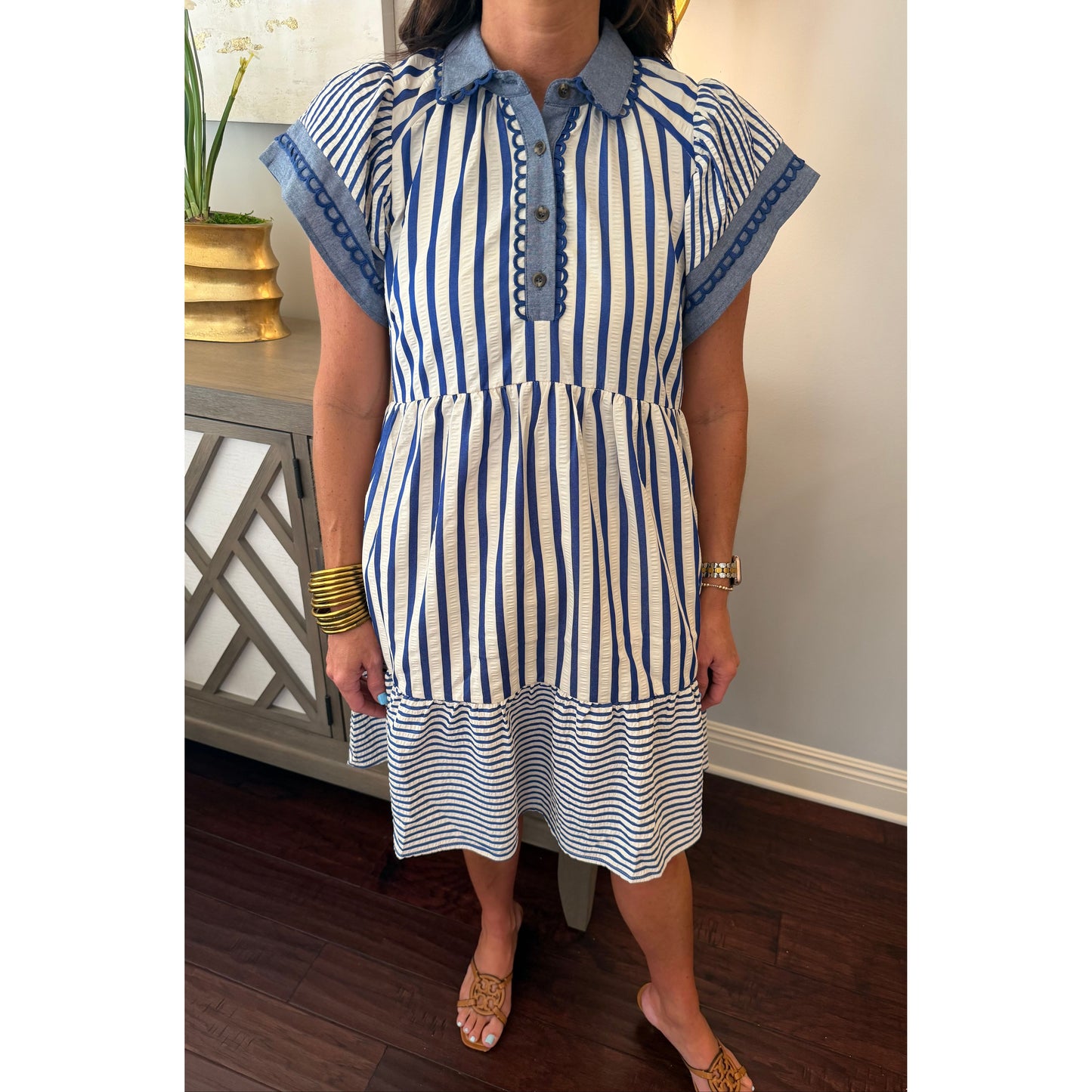 Person wearing a blue and white striped dress with rolled-up sleeves, standing indoors.