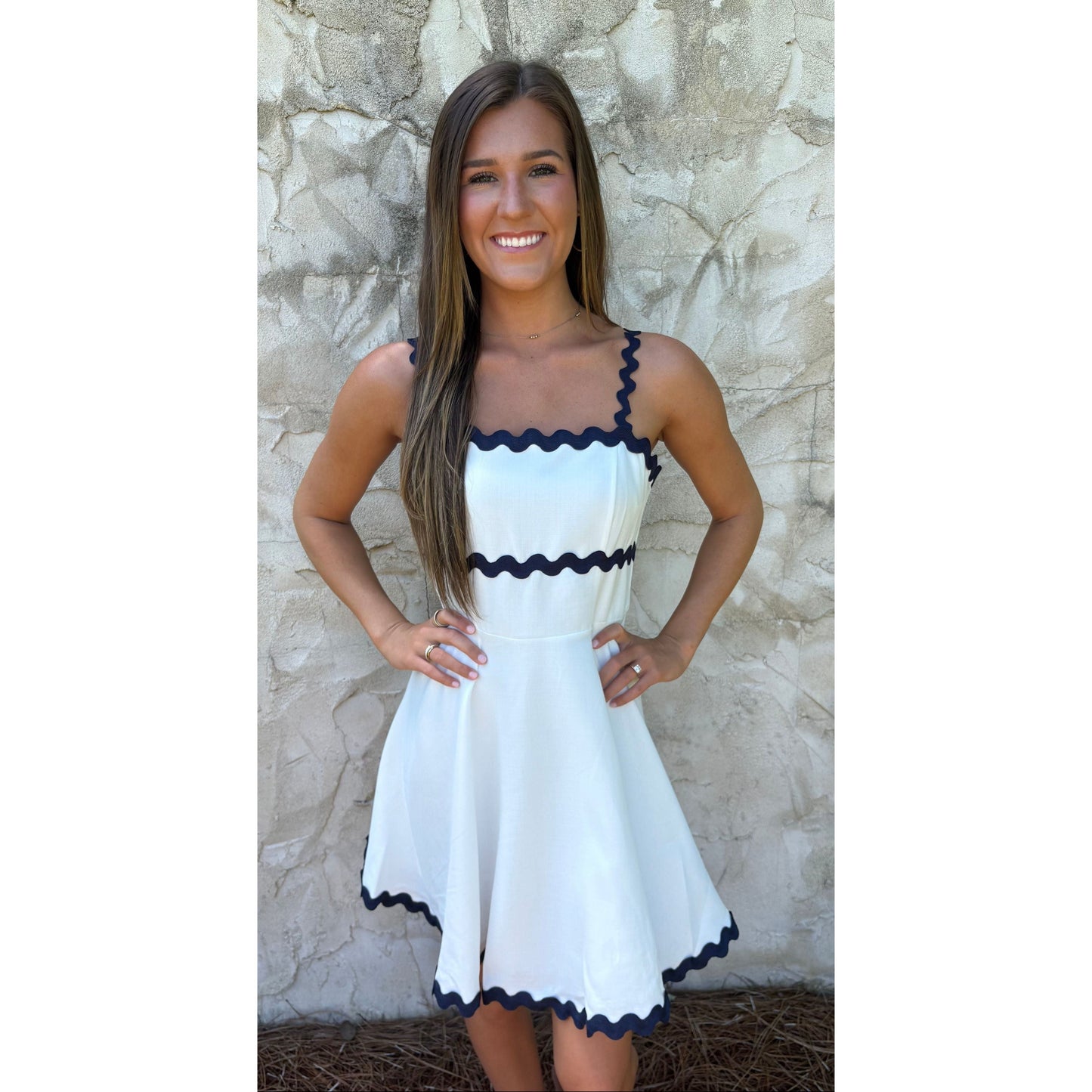 Woman wearing a white dress with black trim against a stone wall.