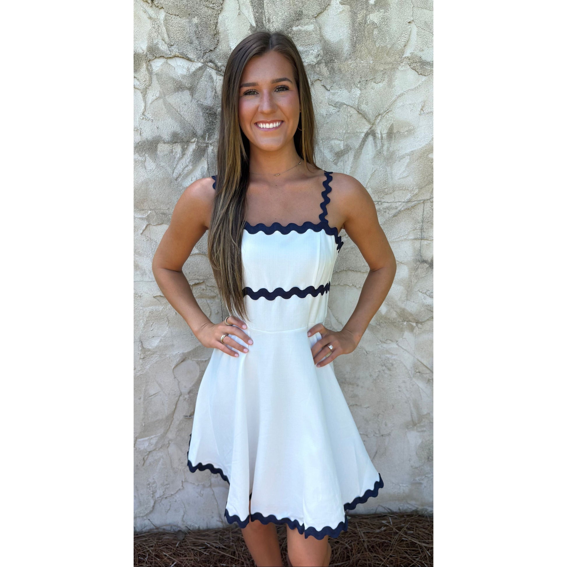 Woman wearing a white dress with black trim against a stone wall.