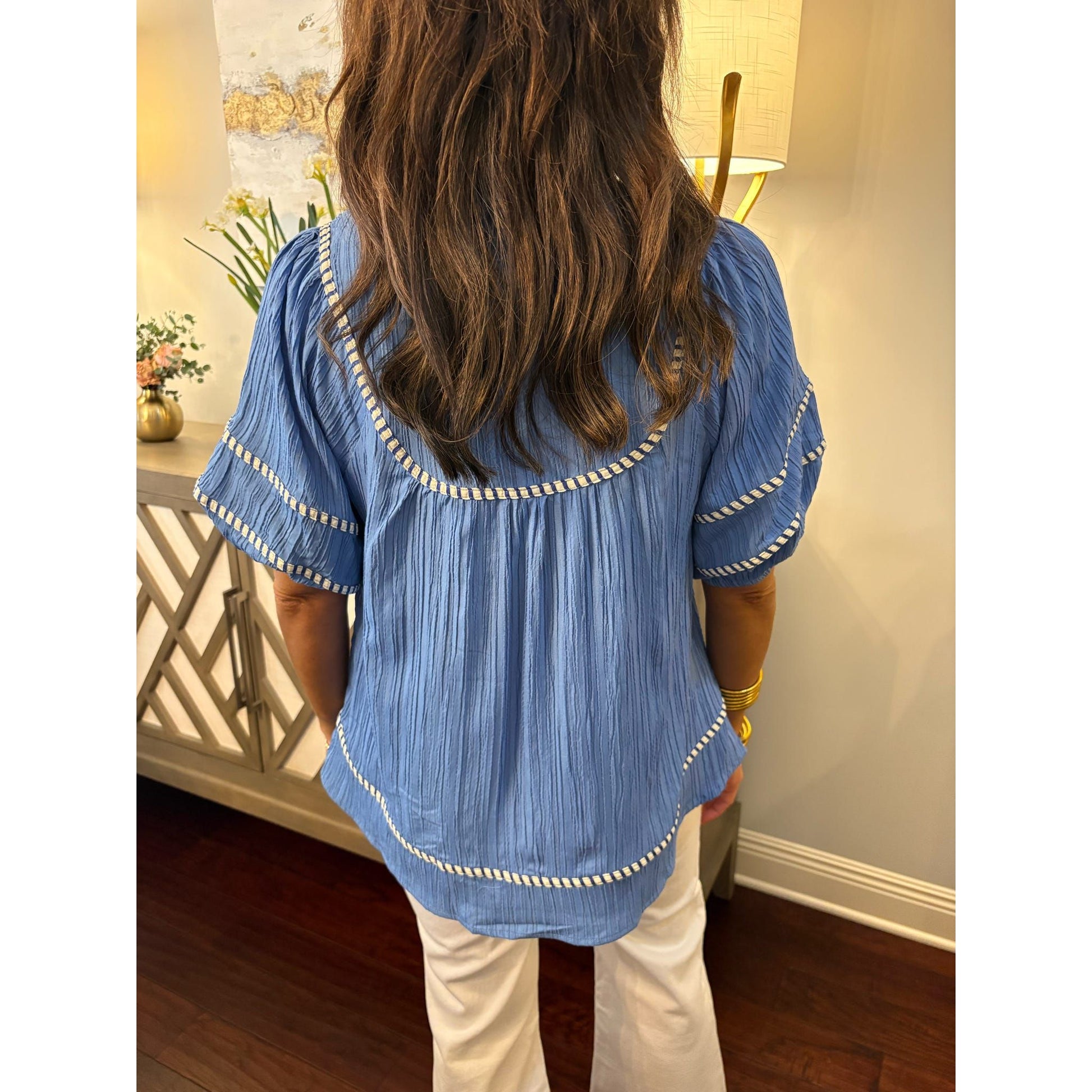 Person wearing a blue blouse with white trim in an indoor setting
