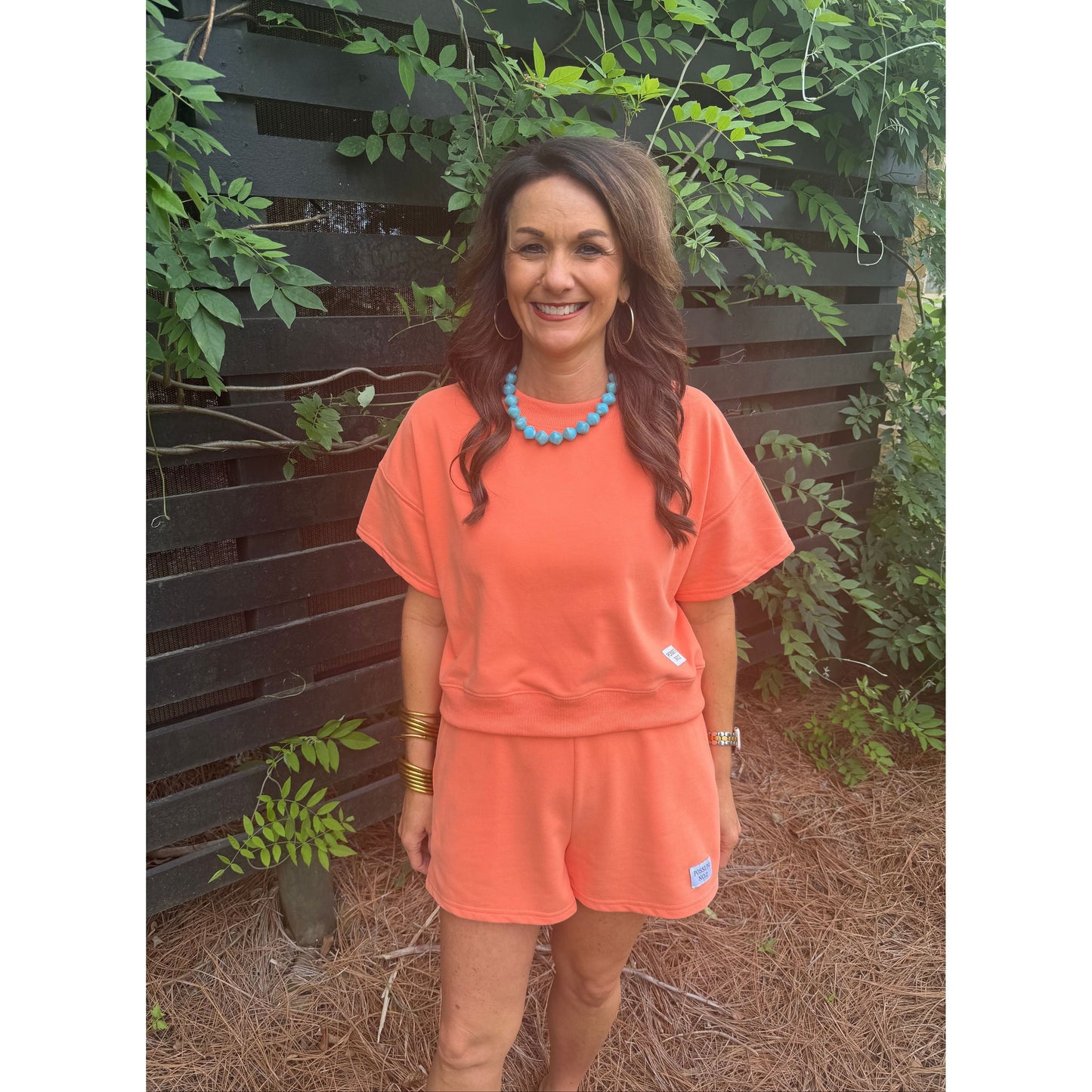 Woman in an orange outfit standing outdoors with greenery in the background