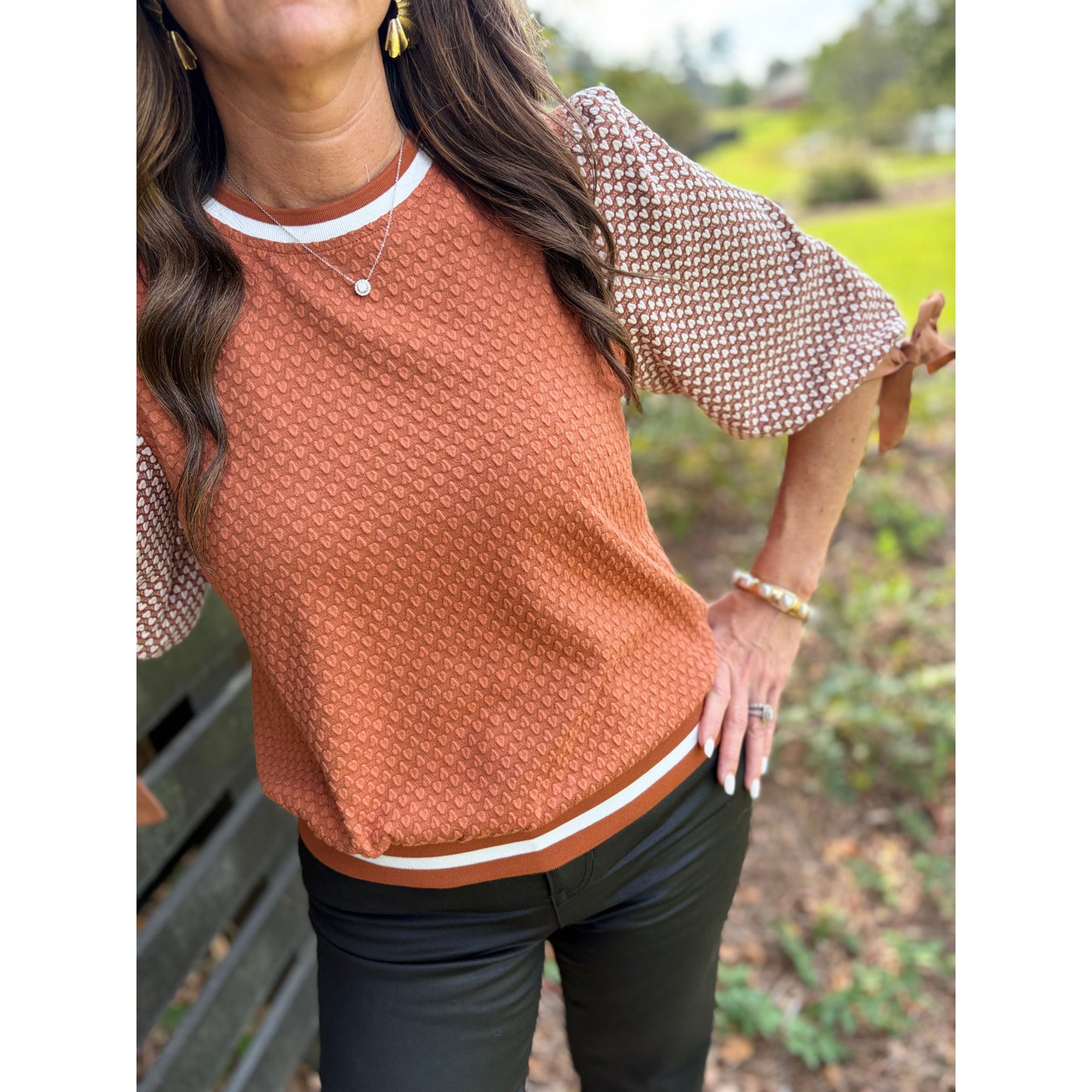 Woman wearing a brown textured top with white trim outdoors