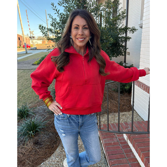 Woman wearing a red sweatshirt and blue jeans standing outside a building.