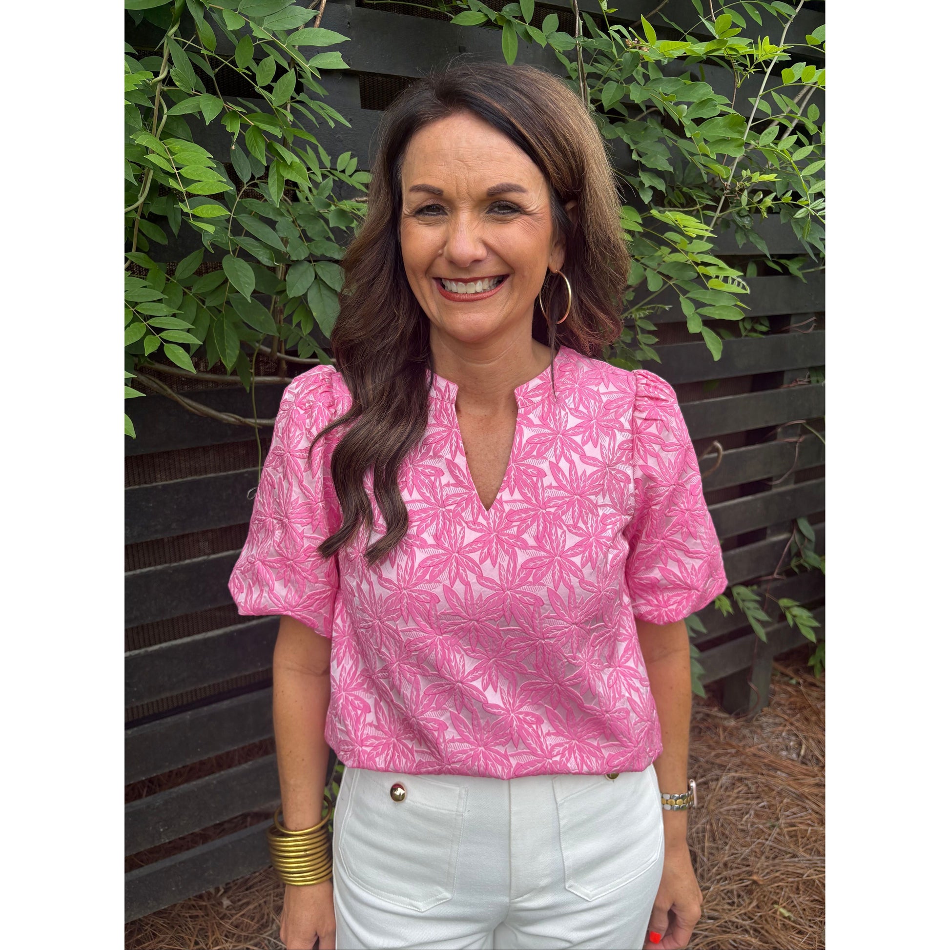 Woman wearing a pink floral jacket sitting outdoors with greenery around