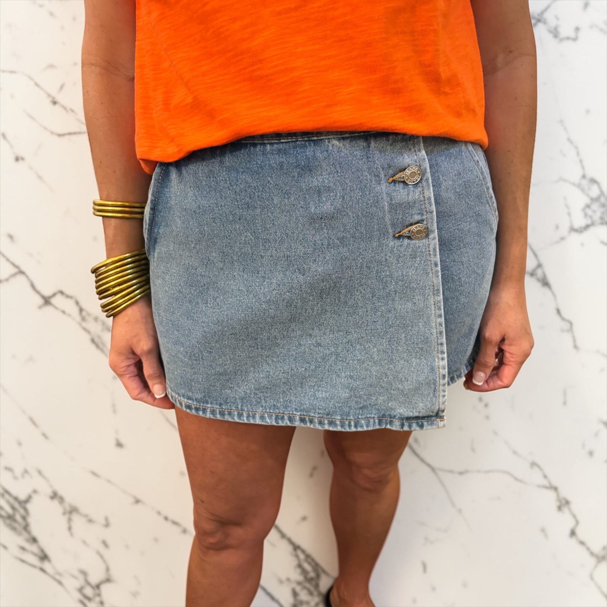 Person wearing an orange top and denim skirt on a marble background