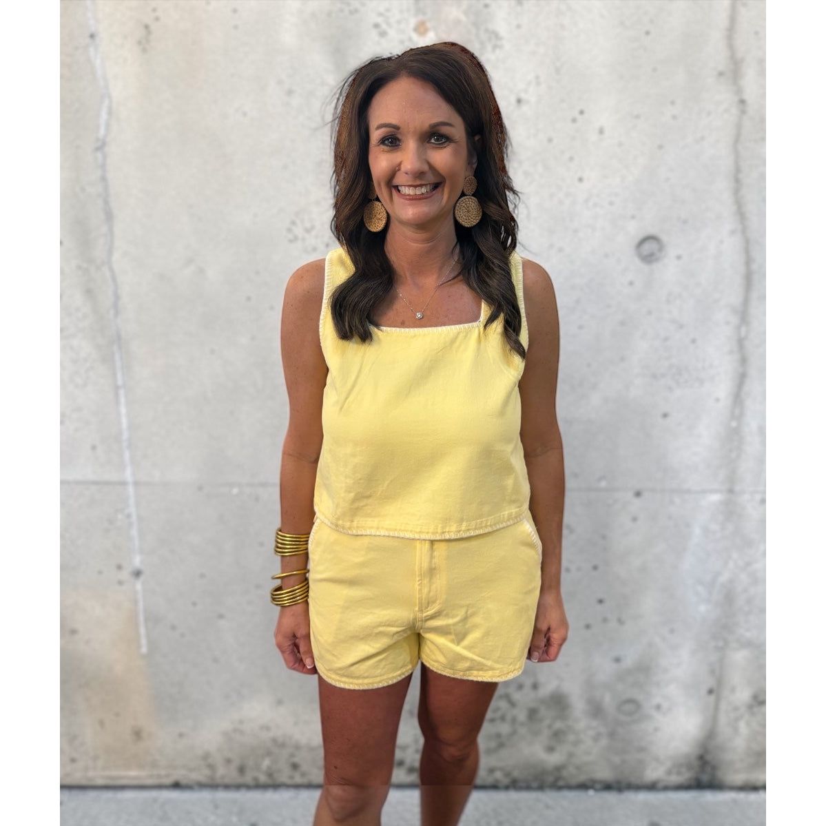 Woman wearing a yellow outfit standing against a textured wall.